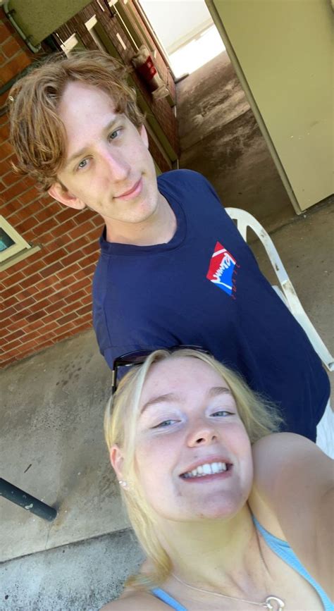 A Man And Woman Sitting On A Chair Outside The Building With Their Arms Around Each Other