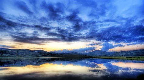 Blue Cloudy Sky Above Calm Body Of Water With Reflection And Landscape