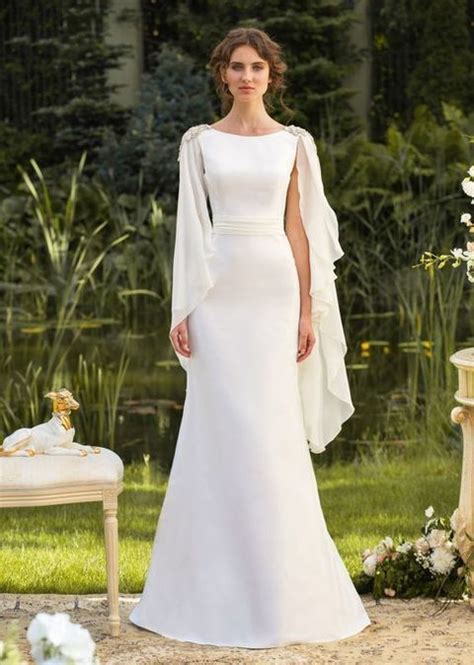A Woman In A White Wedding Dress Standing Next To A Table With Flowers