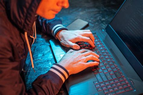 Hooded Hacker Is Typing On A Laptop Keyboard In A Dark Room Under A