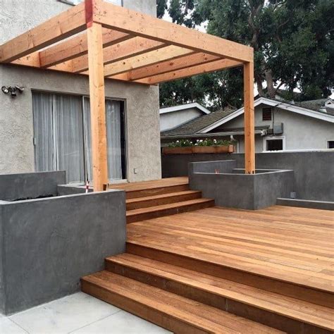 A Wooden Deck With Concrete Planters And Steps Leading Up To A House In