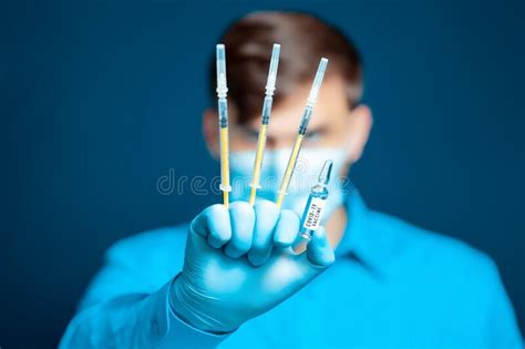 a doctor in a medical mask and gloves in a blue uniform poses with thin syringes between his
