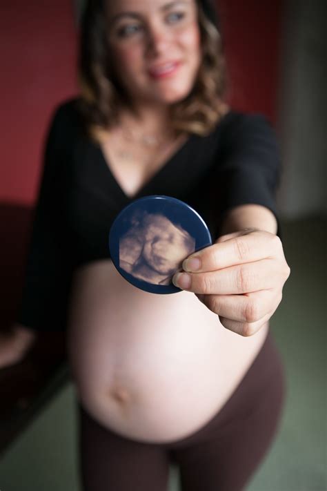 A Pregnant Woman Holding Up A Button With A Photo On It S Side And Smiling