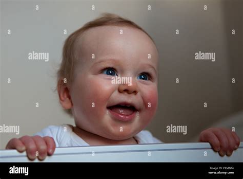 Baby Boy Standing Up Holding On To Teething Rail Of Cot Smiling Stock