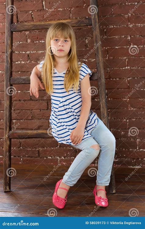 Girl 6 Years Old In Jeans Sits On A Ladder Near Wall Stock Image