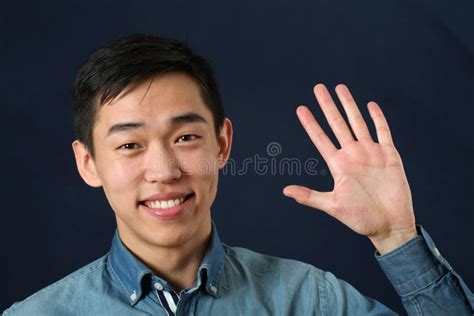 Smiling Young Asian Man Waving His Palm And Looking At Camera Stock