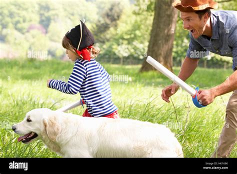 Father Playing Exciting Adventure Game With Son And Dog In Summer Field