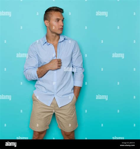 Handsome Young Man In Blue Unbuttoned Shirt And Beige Shorts Posing