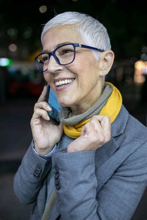 Smiling Mature Senior Woman With Short Gray Hair And Eyeglasses Use Phone On Street Night Scene