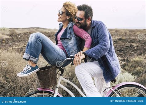 Happy Adult Caucasian Couple Having Fun With Bicycle In Outdoor Leisure Activity Concept Of