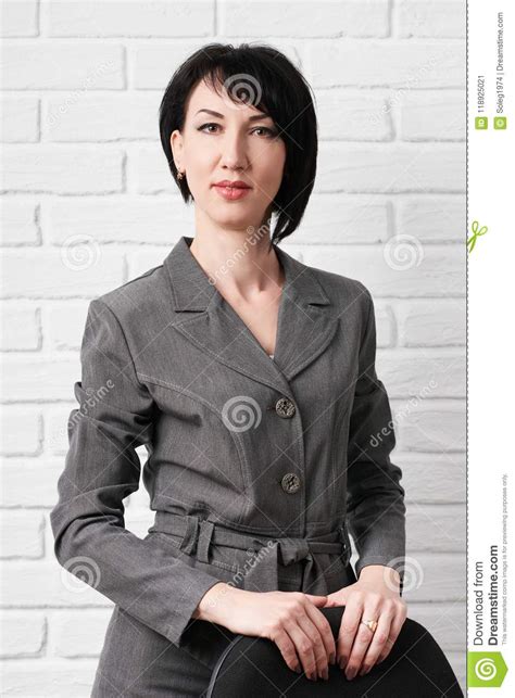 Business Woman Dressed In A Gray Suit Poses With A Chair In Front Of A