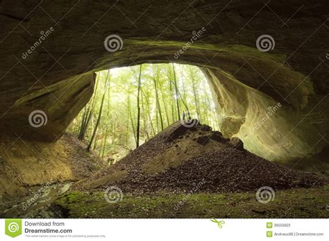 Cave Entrance In Huge Cliff In The Forest With Man Standing In Front