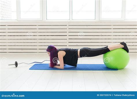 Young Asian Girl With Colored Hair Makes A Plank Exercise Using Fitball On A Blue Sports Mat