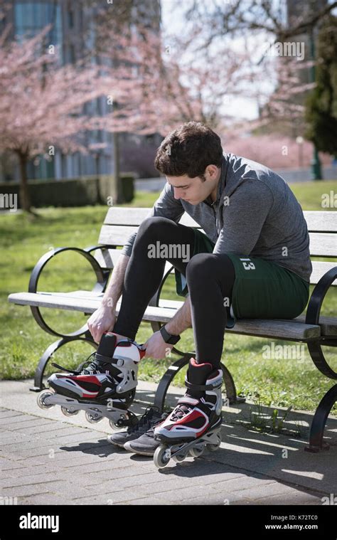 Young Man Wearing Roller Skates While Sitting On Bench At Park During