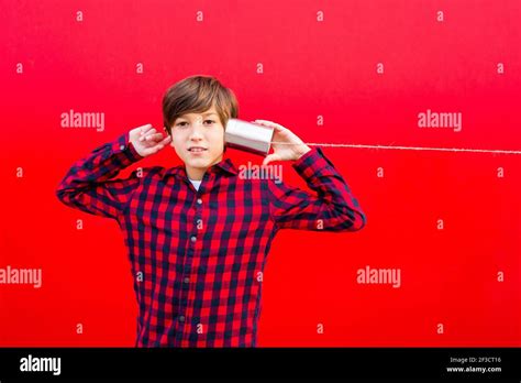 Boy Using Two Metal Cans And A Thread As A Telephone Against A Red Wall