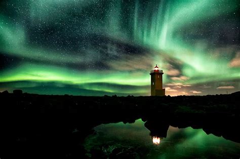 The Aurora Lights Shine Brightly In The Sky Above A Lighthouse