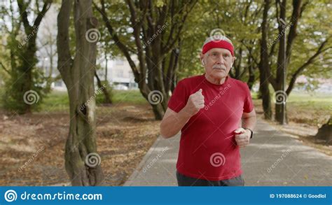 Senior Old Man Running Working Out Cardio In Park And Using Bluetooth