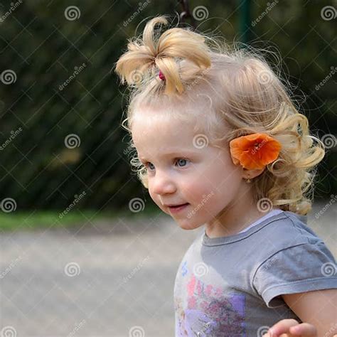 Blond Flicka Med En Orange Blomma I Hår Fotografering För Bildbyråer