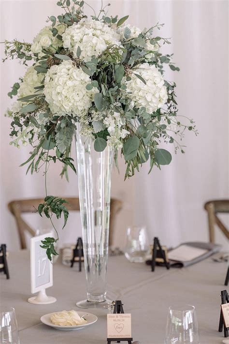 A Vase Filled With White Flowers Sitting On Top Of A Table Next To Wine