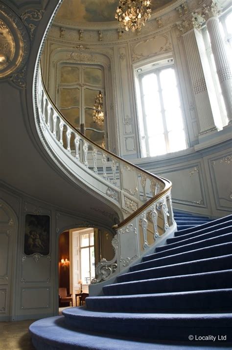 An Ornate Staircase With Chandelier And Blue Carpeted Stairs In A White