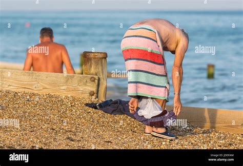 Man On The Beach With A Towel As He Changes Out Of His Swimming Trunks