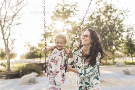 Happy Mother Pushing Cute Daughter Swinging At Playground 11100099910 の