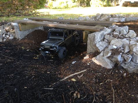 A Toy Truck Parked Under A Wooden Bench In The Dirt Next To Rocks And