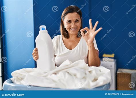 Middle Age Hispanic Woman Doing Laundry Holding Detergent Bottle Doing