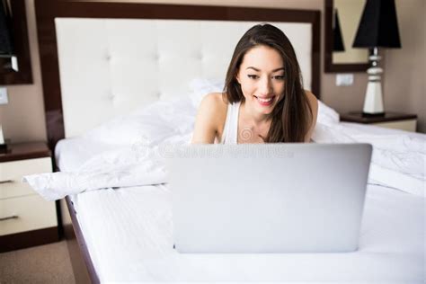 smiling woman catching up on her social media as she relaxes in bed with a laptop computer on a
