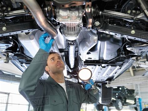 Mechanic Working Under Car In Car Dealership Workshop Holding Torch