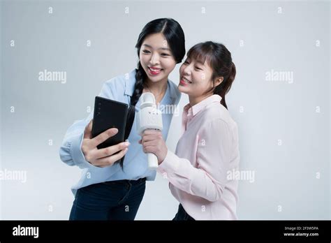 Two Asian Women Sisters Singing With Wireless Mic And Mobile Karaoke Application On Phone Stock