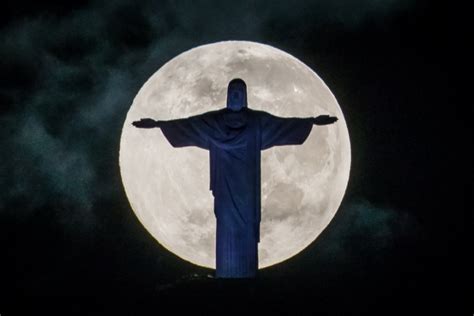 A Full Moon Sets Behind The Christ The Redeemer Statue On Top Of