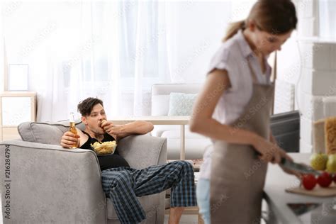 Lazy Husband Watching Tv And His Wife Cooking At Home Stock Foto