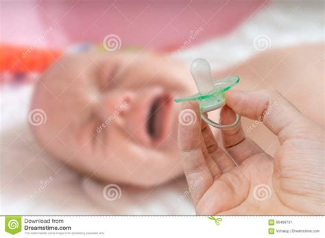 Pacifier In Hand And Crying Baby In Background Stock Image