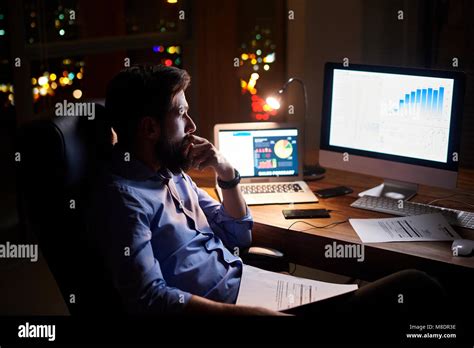 Young Businessman Staring At Computer On Office Desk At Night Stock