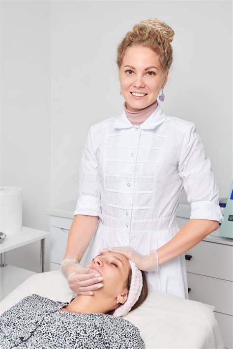 Beautician In Gloves Massages Female Face Skin For Rejuvenation Procedure In Beauty Salon Stock