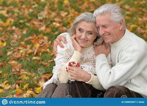 Elderly Couple Sitting Together In The Park On The Grass In Autumn