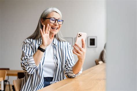 Smiling White Haired Mature Woman Waving Hand And Using Cellphone Stock