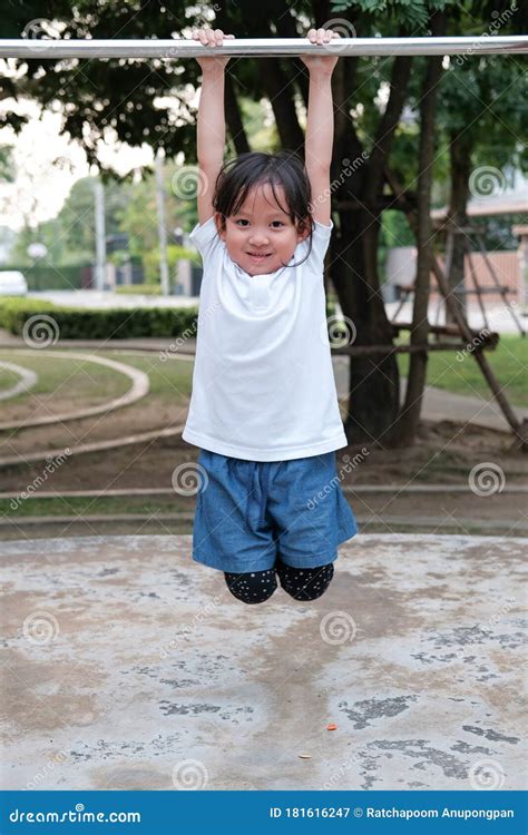 Cute Asian Kid Hanging On Pull Up Bar At Playground In The Village Park