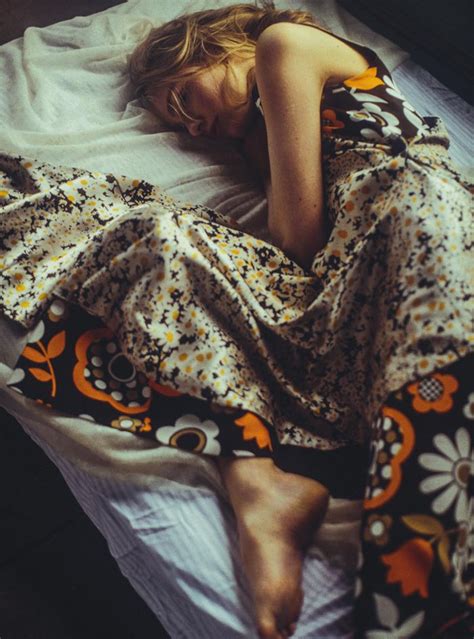 A Woman Laying On Top Of A Bed Covered In A Floral Print Blanket With Her Eyes Closed