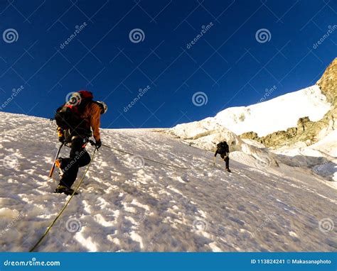 Two Mountain Climbers Headed To A High Alpine Peak Over A Steep Glacier