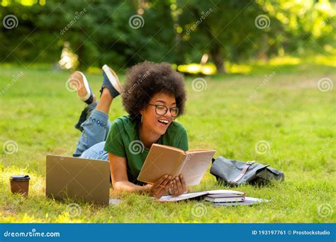 Cheerful African Student Girl Reading Books Outdoors Lying On Lawn In