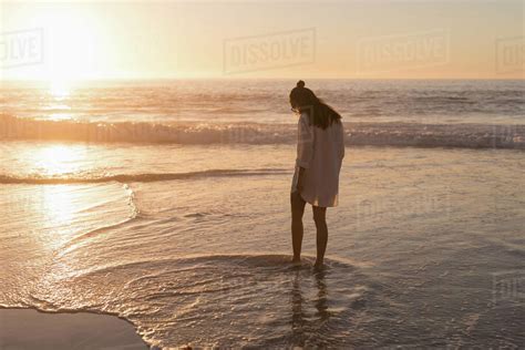 Woman Standing In Sea On The Beach At Dusk Stock Photo Dissolve