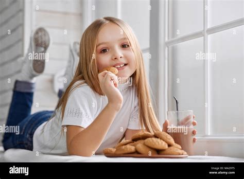 cute girl lies on window sill with cookie plate and glass of sweet delicious chocolate milk