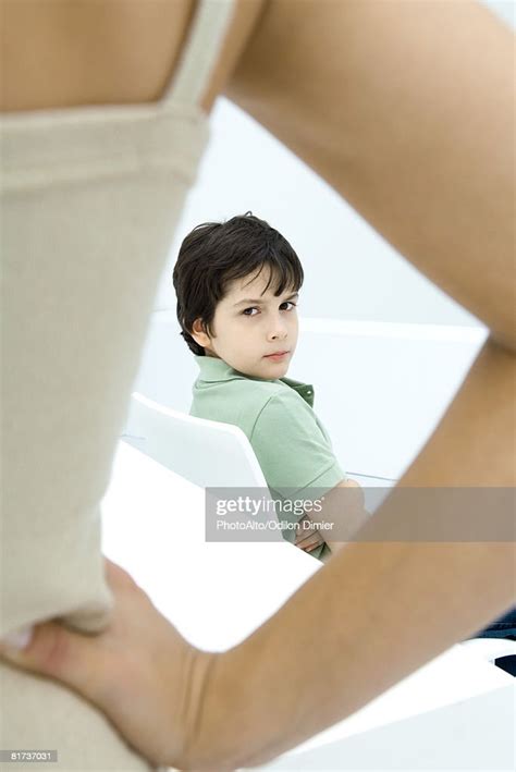 Boy Sulking Looking Over Shoulder At Mother In Foreground With Hand On
