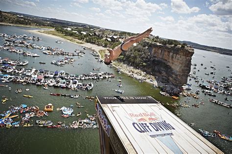 A Man Diving Into The Water From A Ramp In Front Of A Large Group Of Boats