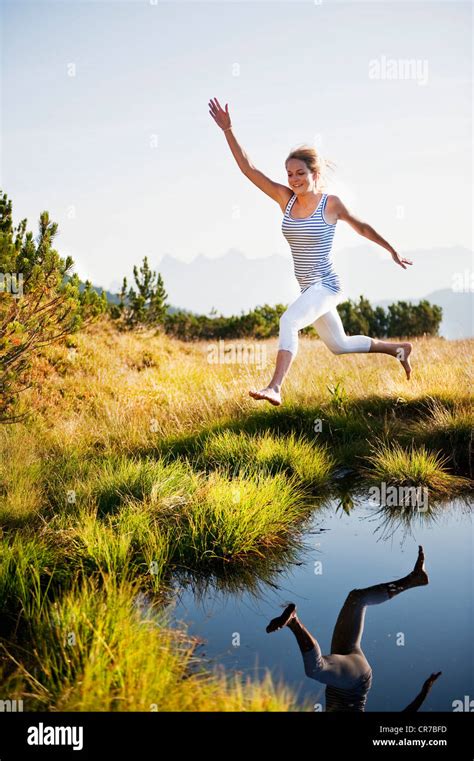 Austria Salzburg County Young Woman Jumping Over Mountain Lake Stock