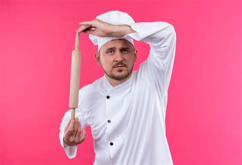 Free Photo Young Handsome Cook In Chef Uniform Holding Rolling Pin Looking Isolated On Pink Space