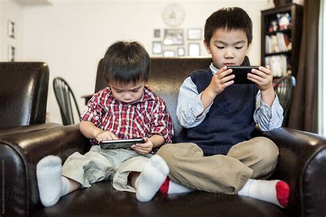 Asian Kids Playing Game At Home On The Cell Phones By Stocksy