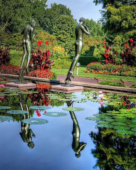 Two Statues Are Standing In The Middle Of A Pond With Lily Pads And Red
